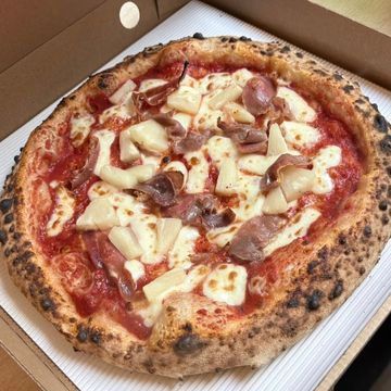 A freshly baked pizza with cheese and ham in a cardboard box.
