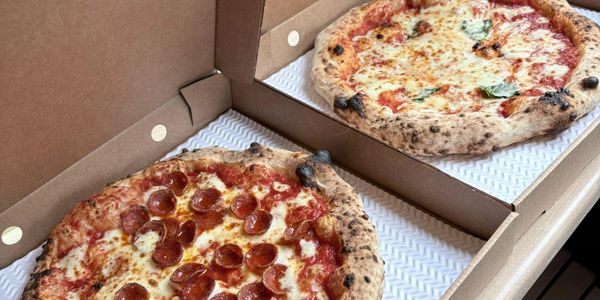 Two freshly baked pizzas in open delivery boxes, one pepperoni and one cheese.