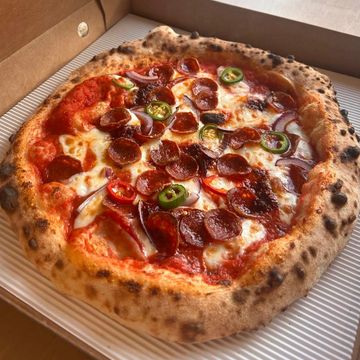 Pepperoni pizza with jalapeños and red onions in a delivery box.