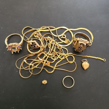 A collection of gold rings, chains, and a heart-shaped pendant on a black surface.