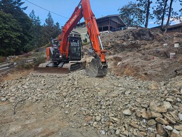 Orange excavator working on rocky terrain near residential houses.