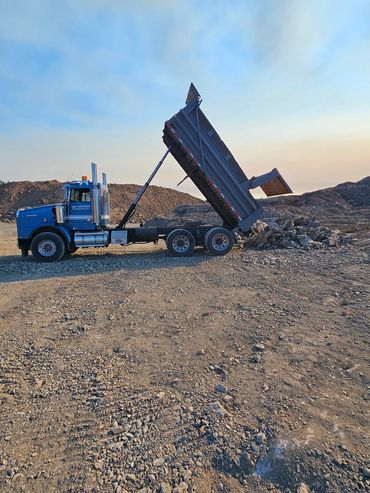 Blue dump truck unloading gravel on a construction site.