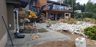 Construction site with a mini excavator and building materials near a house.