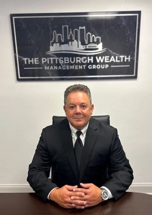 Michael Battalini, Pittsburgh-based retirement planner and CEO of The Pittsburgh Wealth Management Group, seated in his office with the Pittsburgh skyline logo behind him.”