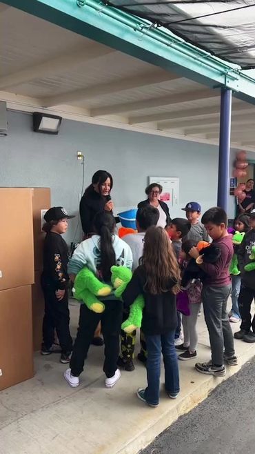 Woman speaking to children holding green stuffed frogs in a line outdoors.