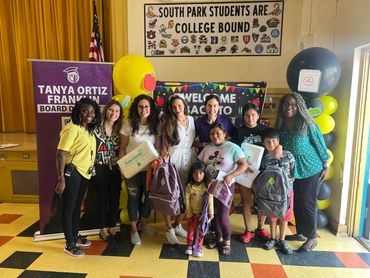 Group of smiling adults and children at a school event with backpacks and gifts.
