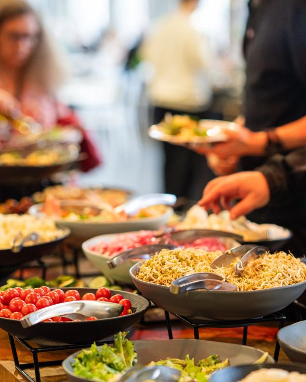 Buffet with fresh salad ingredients and people serving themselves.