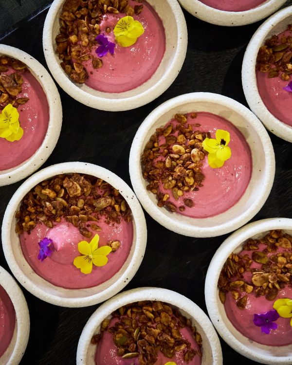 Bowls of pink smoothie topped with granola and edible flowers.