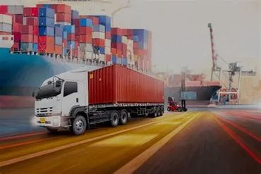 A truck carrying a red shipping container at a busy port with stacked containers.