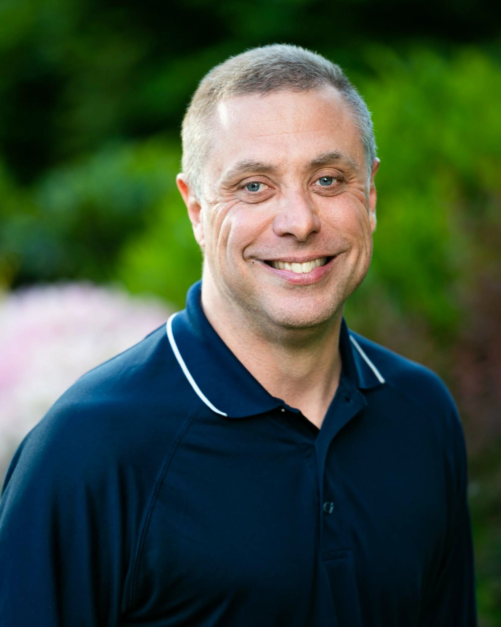 Smiling man in a navy blue polo shirt with a blurred green background.