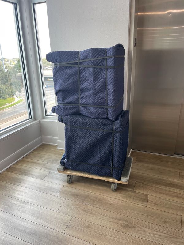 Two large items wrapped in blue moving blankets on a wooden dolly.