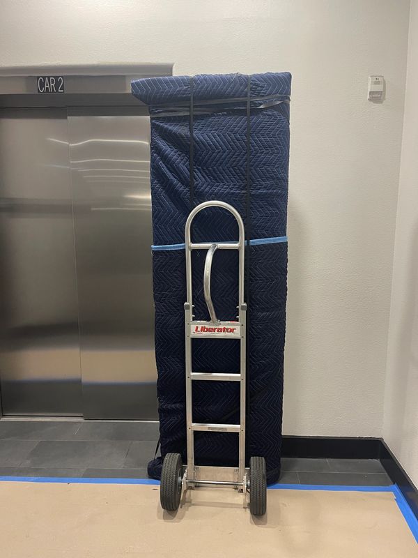 Hand truck carrying a large, wrapped item near an elevator labeled CAR 2.