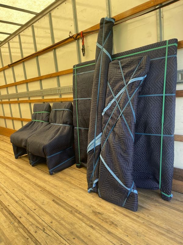 Furniture wrapped in protective moving blankets inside a truck.