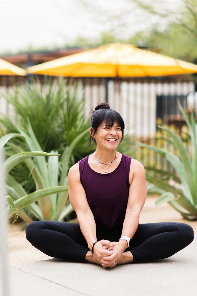 Private Yoga instructor Karen wearing purple top and smiling while in a stretching position outdoors.