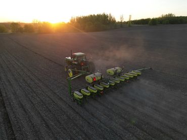Tractor planting seeds on a farm field at sunrise.