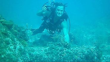Bradley Williamson scuba diving in front of a coral encrusted cannon from a shipwreck.