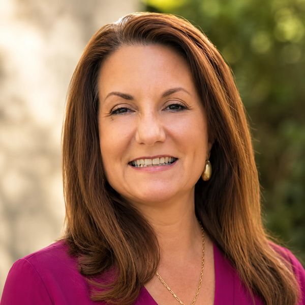 Smiling woman with long brown hair in a magenta top outdoors.