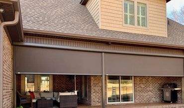 Patio area with retractable brown shades on a brick house.