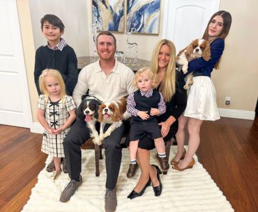 Family sitting in front of piano holding Cavalier King Charles dogs