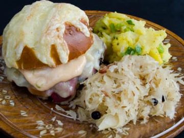 Reuben sandwich on a pretzel roll with cheese , german potato salad and sauerkraut.