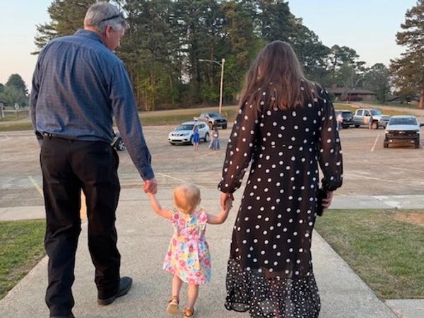 A couple holding hands with a toddler walking outdoors.