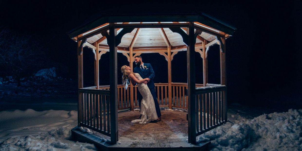 Couple dancing in a lit wooden gazebo at night with snow.