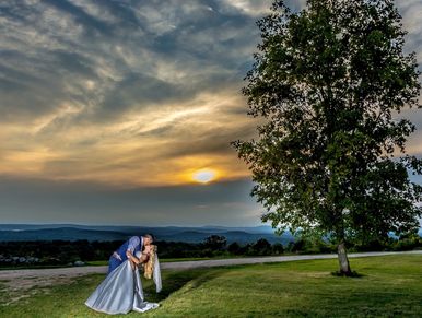 Groom dips the bride for a kiss in front of a glowing sunset. At the Vista of Maine Wedding venue