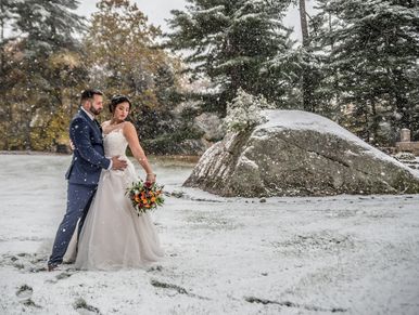 A bride and groom posing in a snowy scene. The bride is looking down her arm at her flowers