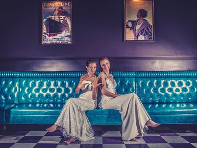Brides of a same sex marriagein a colorful booth showing off rings at the Essex Room wedding venue