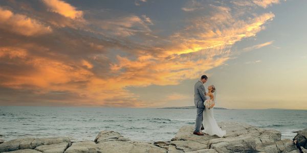 Bride and groom at the waters edge on Peaks Island with dramatic sky from the sunset- Jones Landing
