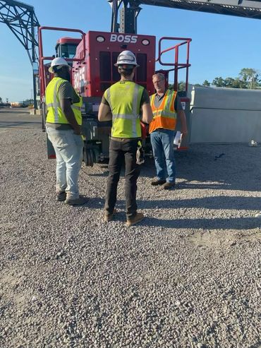 Three workers in safety vests and helmets stand near a red machine labeled BOSS.