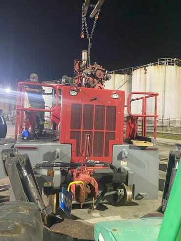Nighttime maintenance on a large red industrial vehicle with a suspended engine.