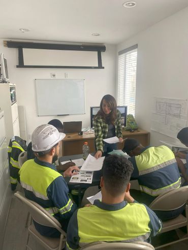 A woman distributes papers to workers in high-visibility uniforms during a meeting.