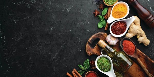 Colorful spices, herbs, and oil arranged on a dark background with a wooden board.