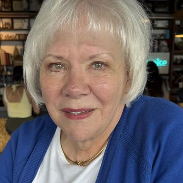 Elderly woman with white hair wearing a blue cardigan and white shirt.