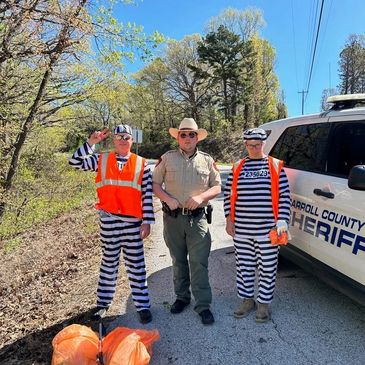 Two people in prisoner costumes with a sheriff on a roadside cleanup.