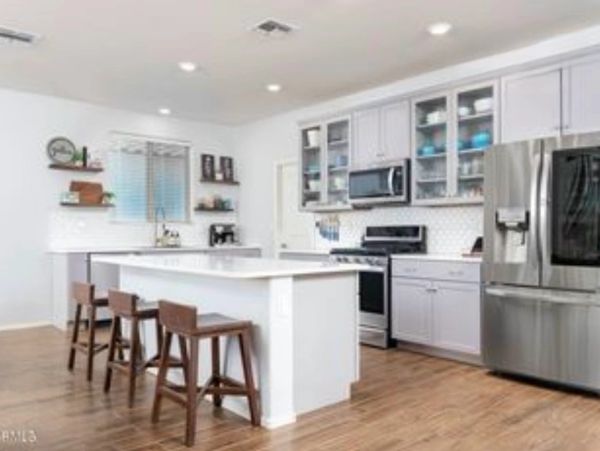 Modern kitchen with white cabinets, stainless steel appliances, and wooden stools at the island.
