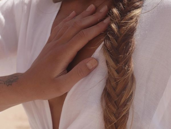 Hand resting gently on a white shirt with a long braided hair.