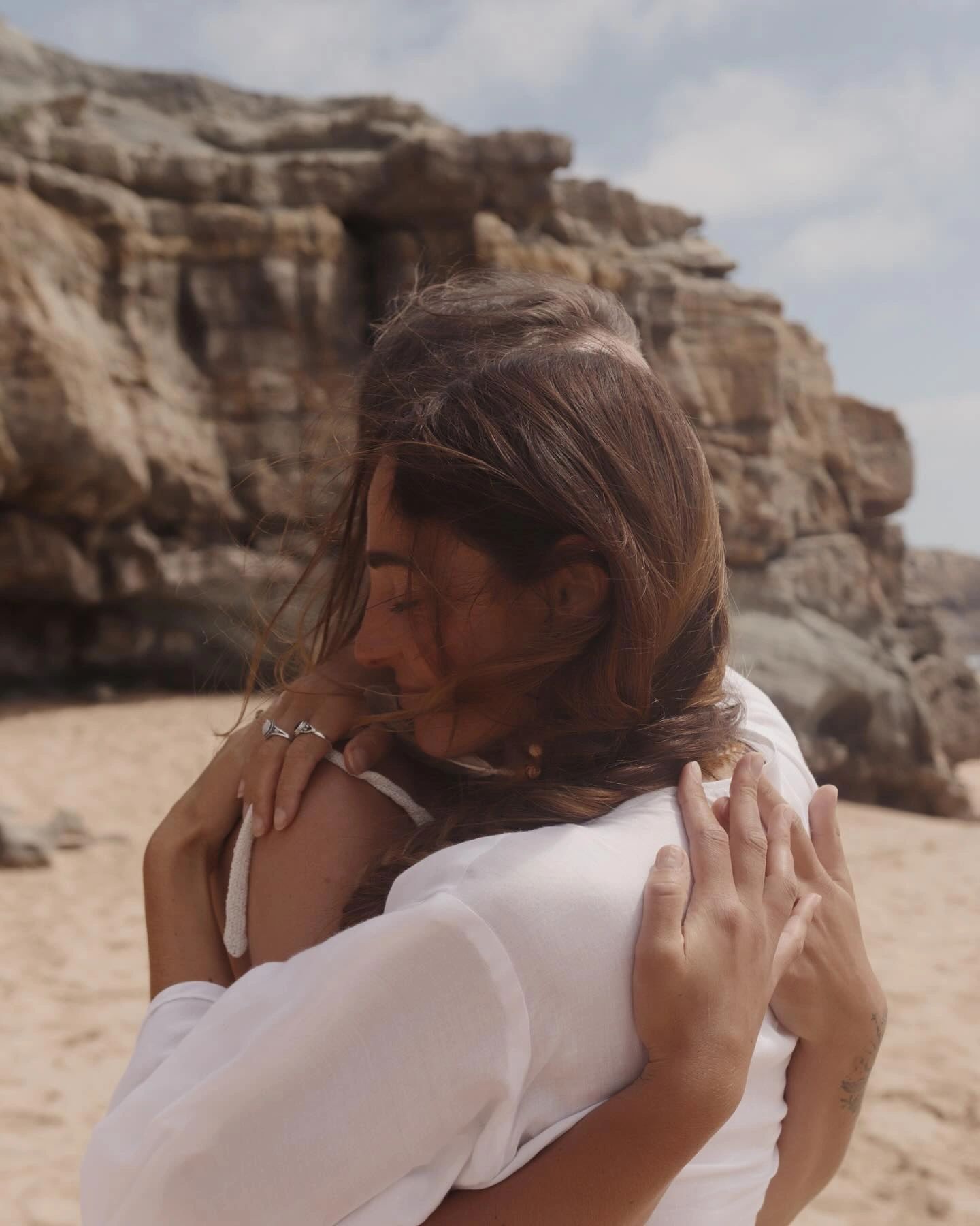 Two people sharing a warm embrace on a rocky beach.