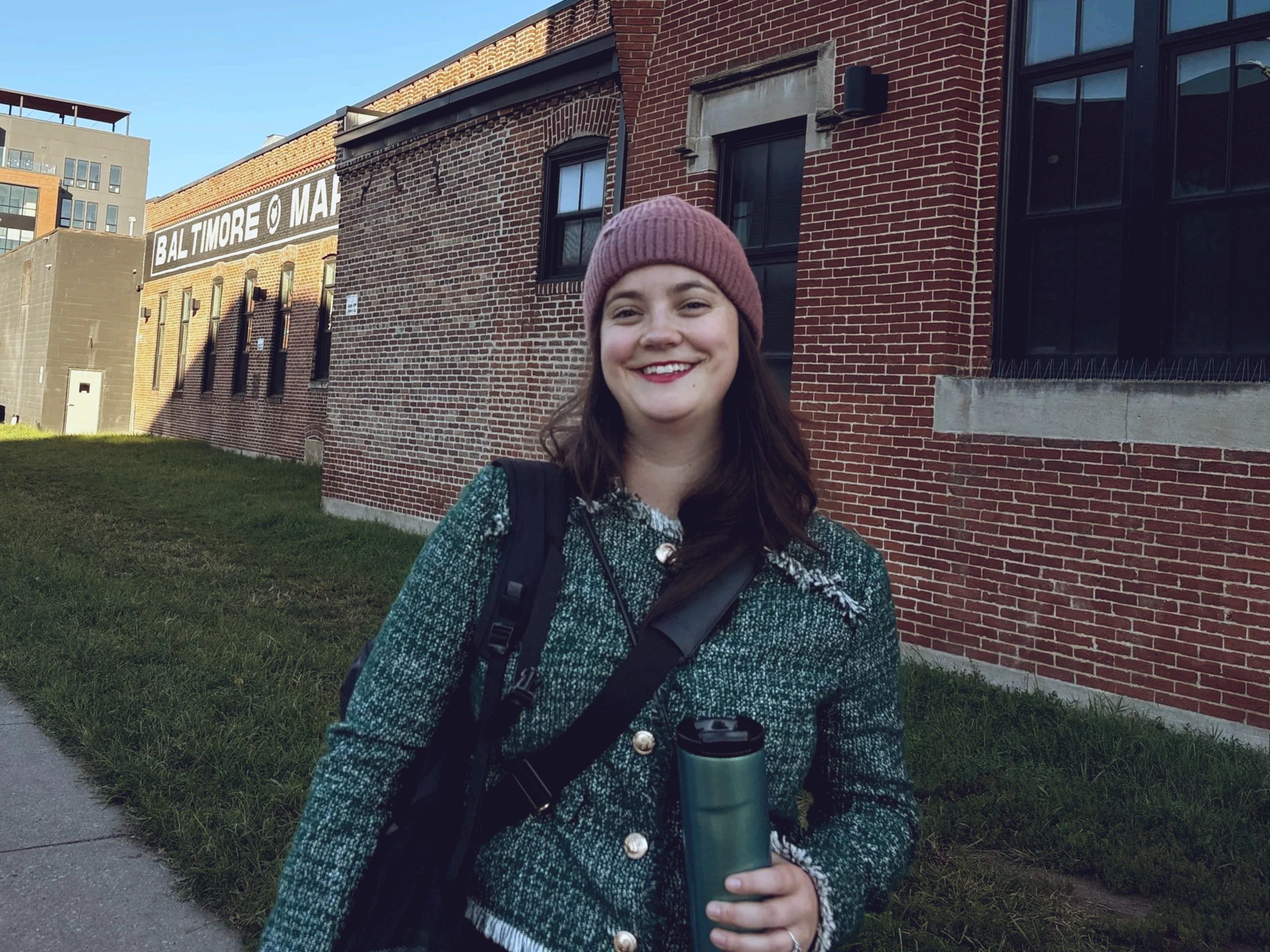 white woman with brown hair smiles as she carries her bags and coffee into the office on a cold day