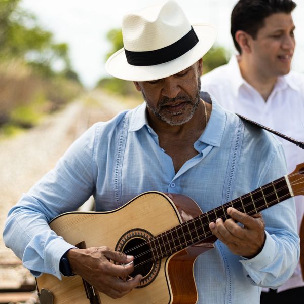 Man in white hat playing acoustic guitar outdoors.
