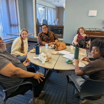 A diverse group sharing a meal and smiles around a table in a cozy room.
