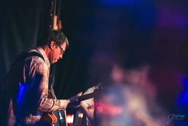 Man playing guitar on stage with focused expression and moody lighting.