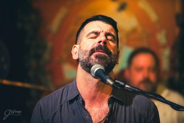 Man passionately singing into a microphone with eyes closed.