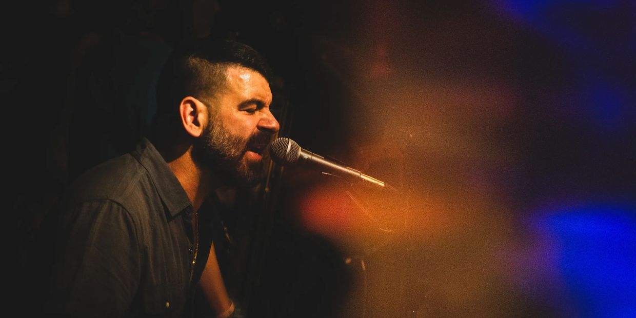 Man passionately singing into a microphone on stage.