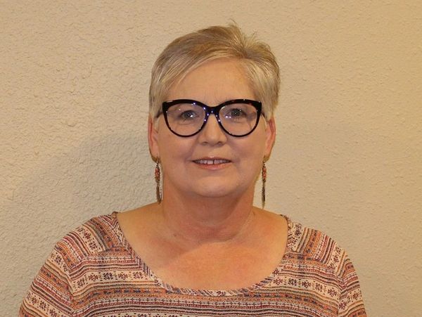 Woman with short blonde hair and glasses smiling against a beige wall.