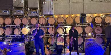 Two singers performing in front of wine barrels at a winery event.