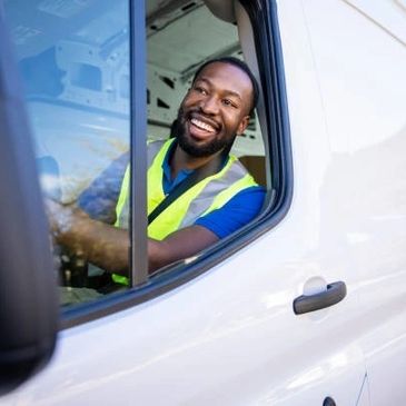 Smiling delivery driver in a white van wearing a safety vest.