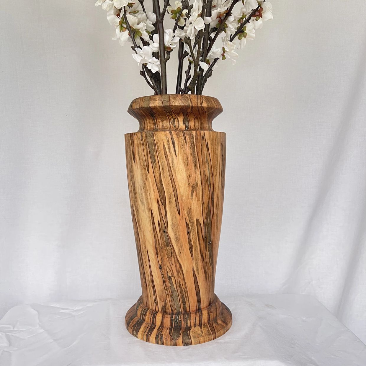 Tall wooden vase with white flowers against a white backdrop.
