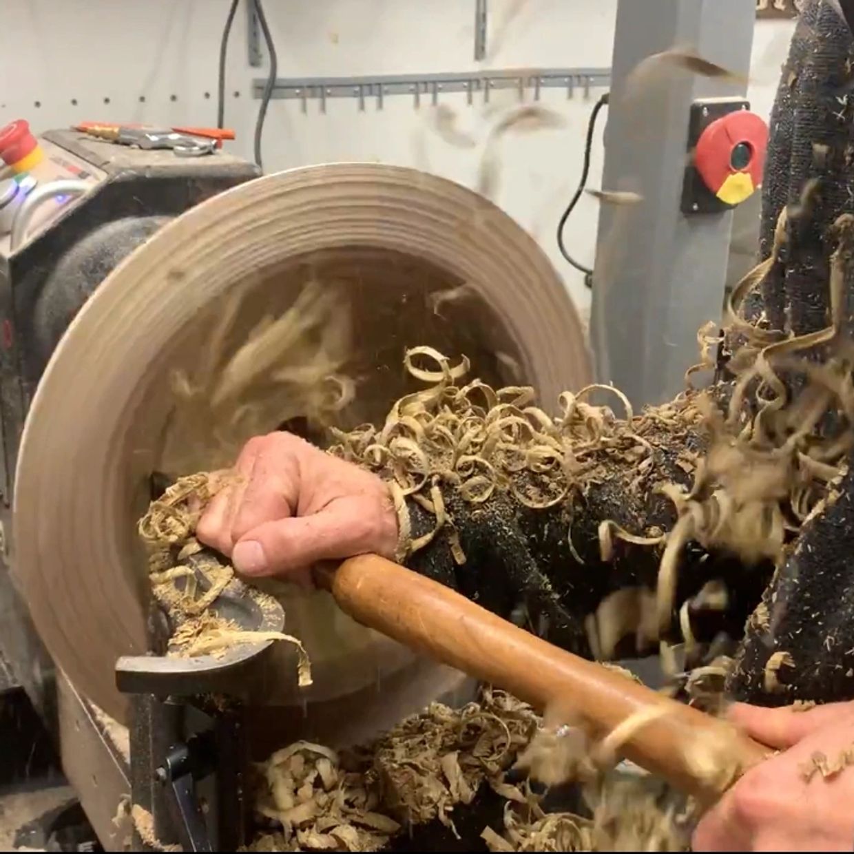 Close-up of a person woodturning on a lathe, with wood shavings flying.